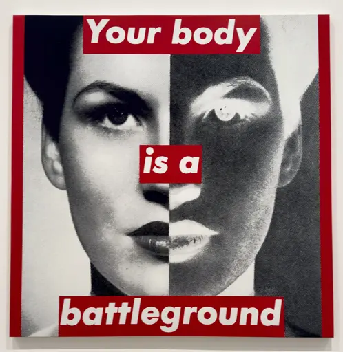 A photograph of a woman that is split down the middle, with half a normal black and white photograph, and the other half inverted. The photo is bordered on both sides by bright red, and white text on bright red says “Your body is a battleground”